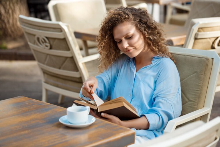 Young beautiful girl reading book, sitting in cafe.