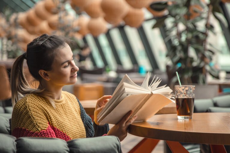 Young beautiful woman in orange sweater reading interesting book in cafe. The concept of reading